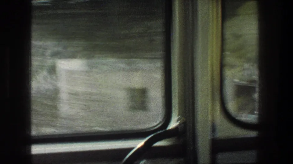 Final 1976 Jerusalem-area vehicle-window frame, with a blurred roadside structure, green hillside, and interior trim.