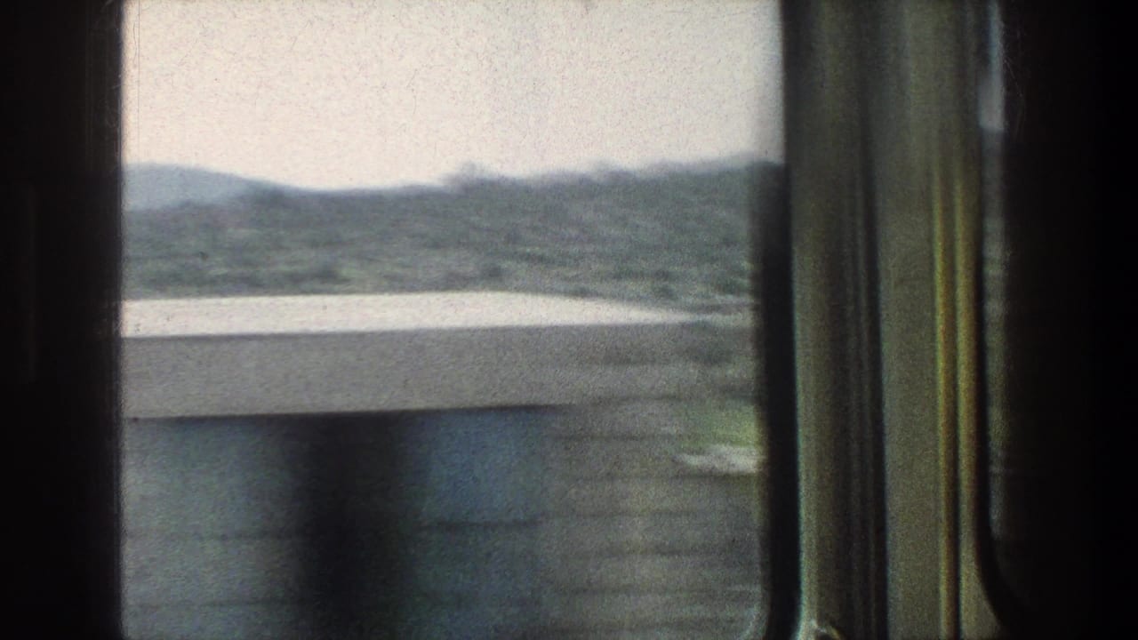 View through a moving window toward hills, water, and the edge of a city street.