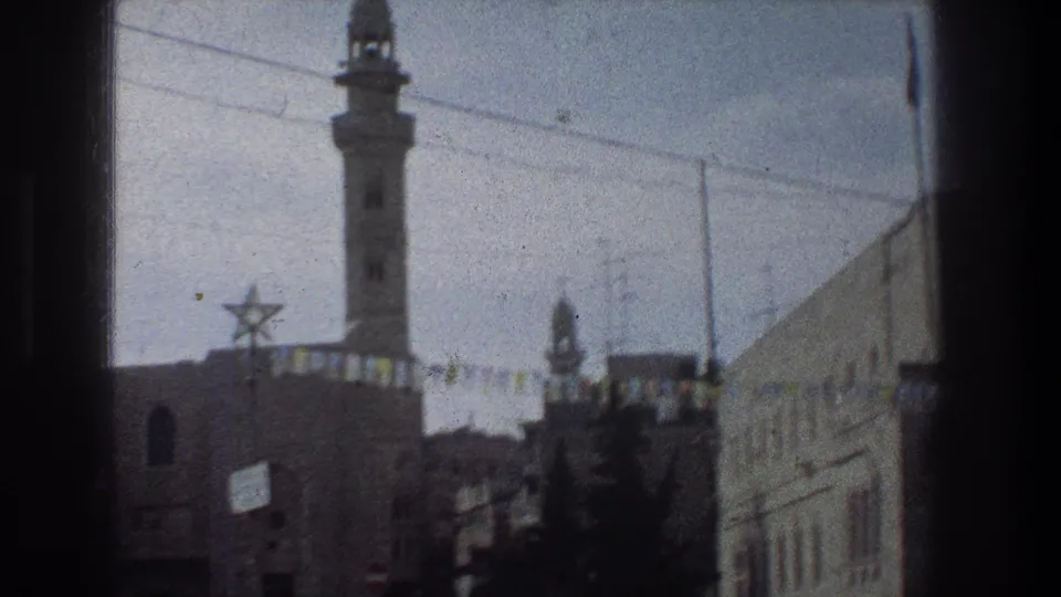 1976 Jerusalem home-movie frame showing a minaret above stone buildings, a Star of David decoration, overhead wires, and dark window framing.