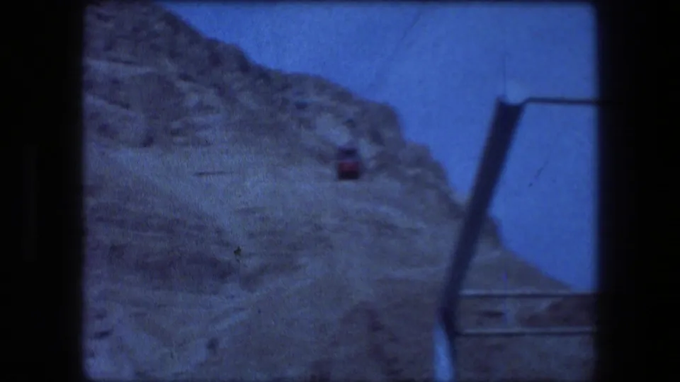 Messada travel footage shows a cable-car or lift line against a steep brown slope and clear blue sky.