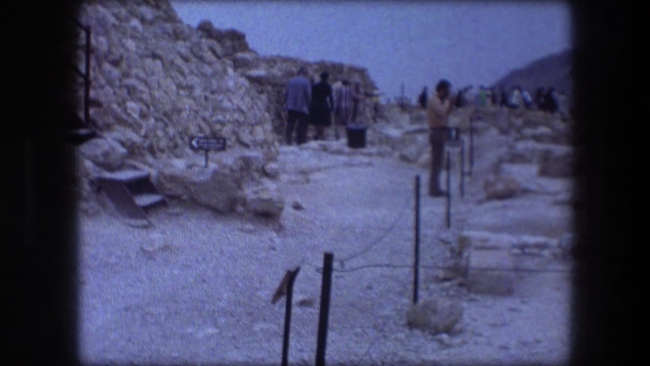 Handheld 1976 Messada footage shows tourists near rough stone walls, a marked path, and a small cistern sign ahead.