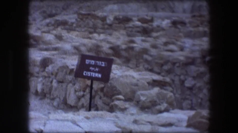 Close view of a cistern sign at Messada, Israel, with Hebrew and English text beside rocks and ruin masonry.