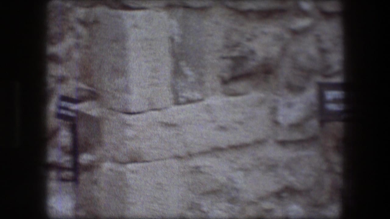 Soft 8mm frame of stone ruins with a partially visible sign near the left edge.