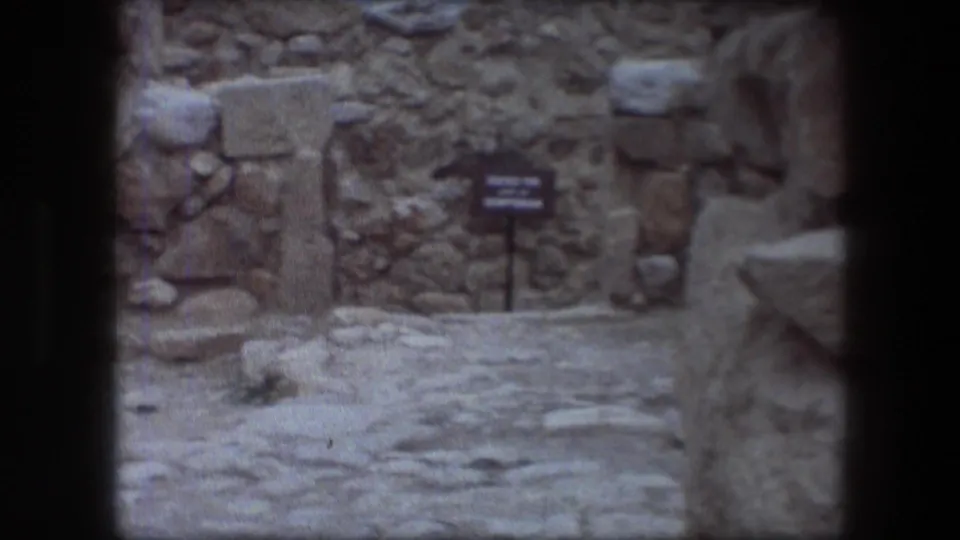 1976 Messada, Israel visitor-shot frame showing a stone walkway, rough ruin walls, and a small bilingual sign ahead.