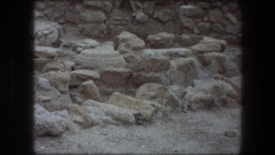 Messada archaeological ruins seen in a grainy 8mm frame, with stones and rough masonry filling the view.