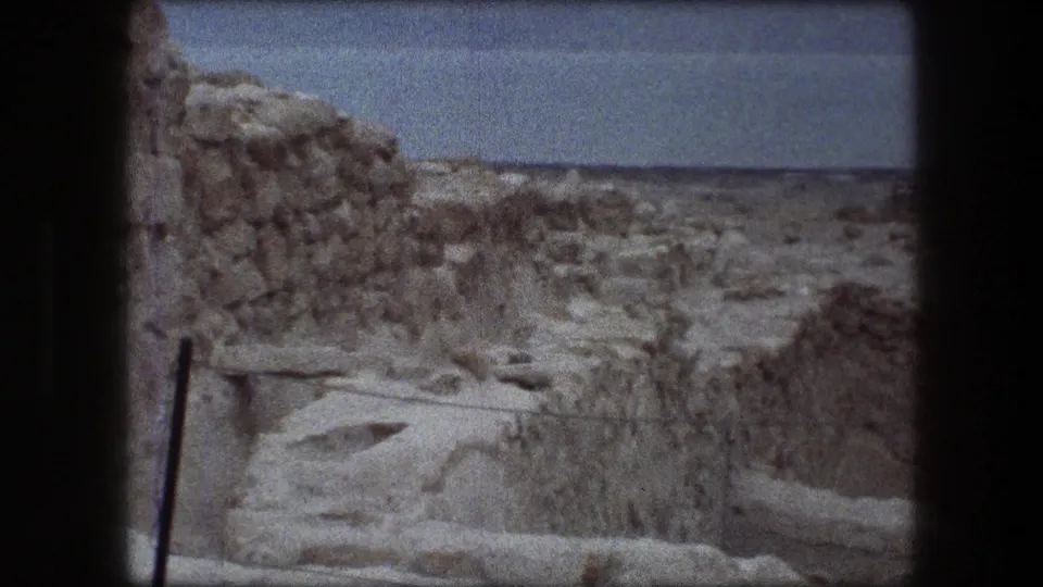 1976 8mm view of weathered stone walls and arid terrain at Messada, Israel, with a distant horizon under a pale sky.