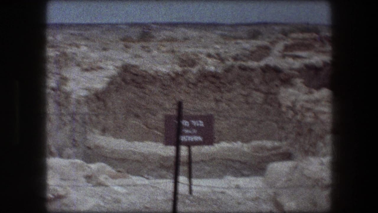 Messada, Israel ruins seen on 8mm film, with a dark bilingual-looking site sign standing before eroded stonework and desert ground.