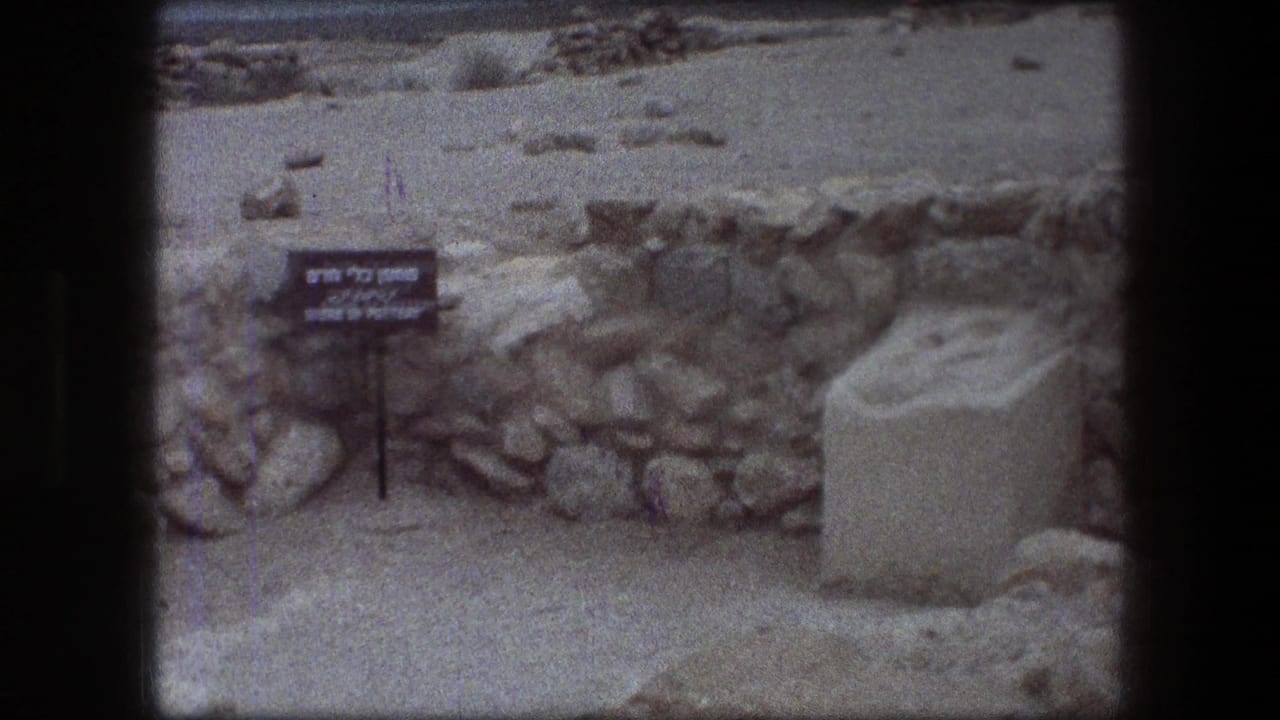 1976 Messada visitor footage showing a pottery exhibit sign, rough stone wall, sand, rocks, and a pale rectangular block.