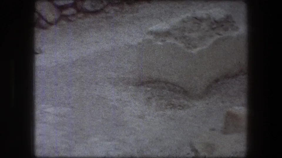 1976 Messada visitor-shot view of a pale stone block and surrounding sand, with rough masonry partly visible at the edge.