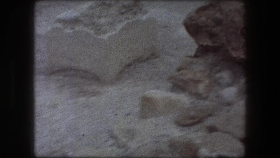 1976 Messada footage showing sandy excavation ground, scattered rocks, a pale block, and rough stone edges during a pan.