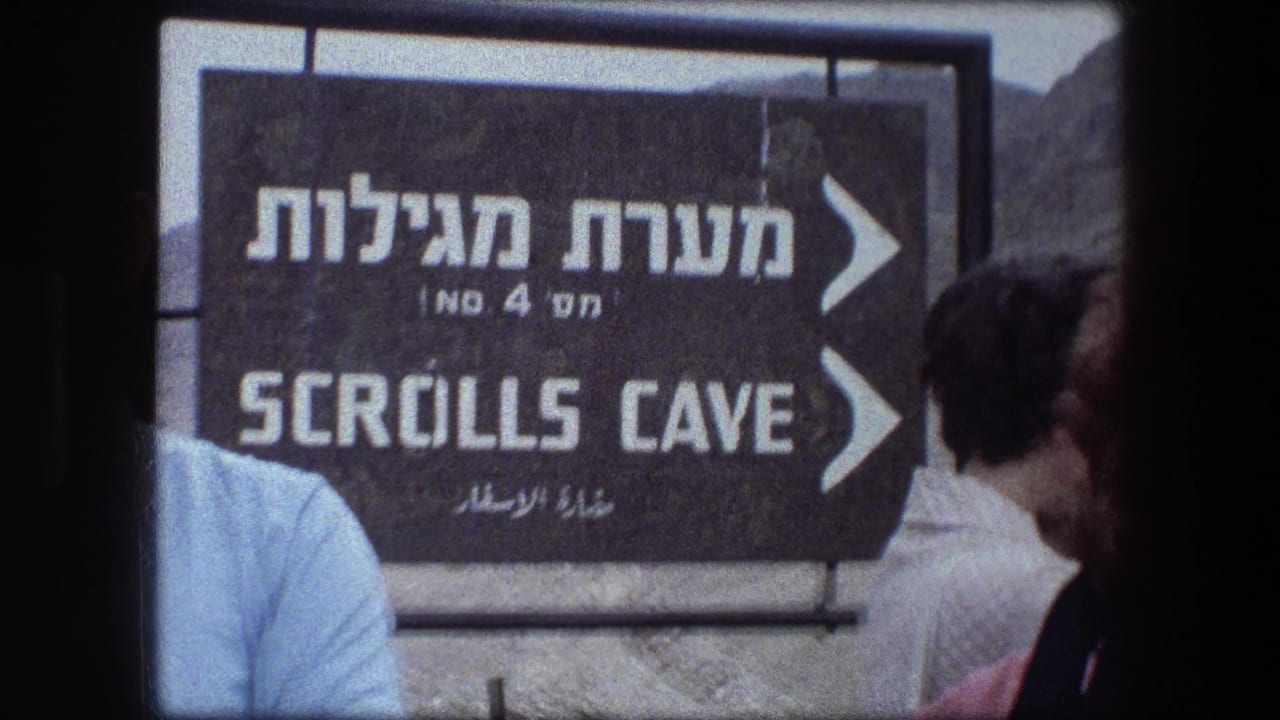Multilingual Scrolls Cave sign with tourists partly visible in front.