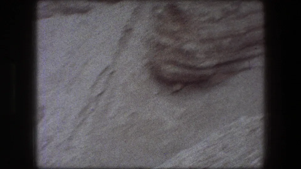 Handheld 8mm view of pale layered rock near the Scrolls Cave area, with no people visible in this frame.