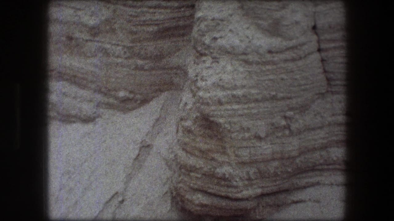 Layered pale rock face with eroded ridges and dark film borders.