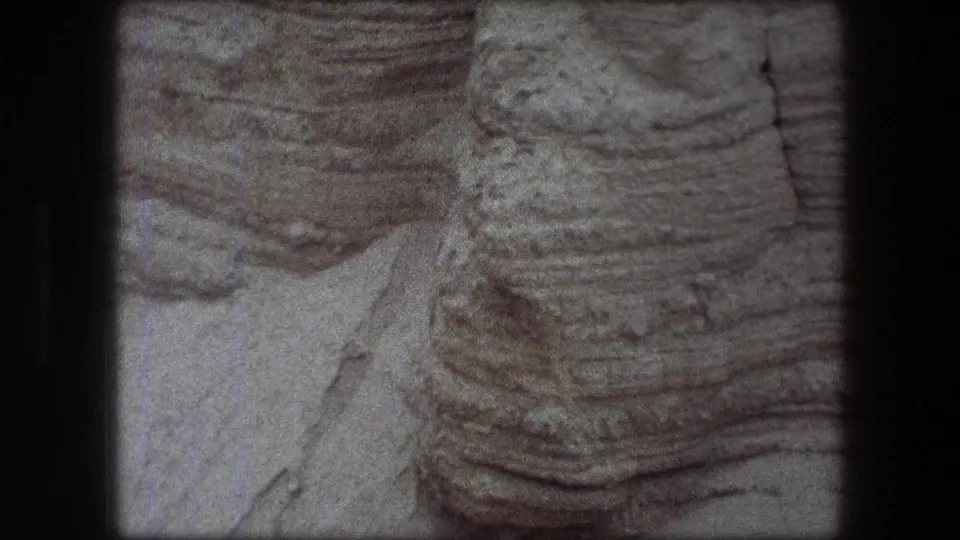 1976 8mm frame from Messada, Israel, showing a close view of stratified pale rock and eroded cliff texture.