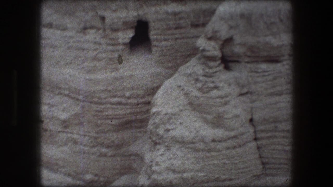 Rocky cliff surface with a small dark cave opening near the upper center.