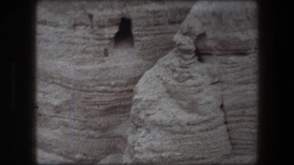 1976 8mm Messada-area view of layered desert rock with a small shadowed opening in the cliff.