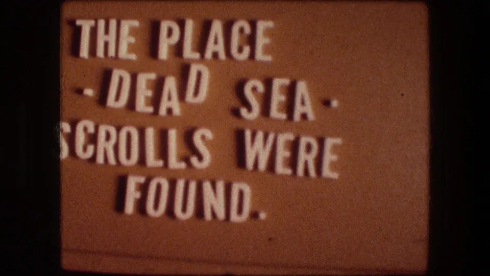 1976 Israel home-movie title card with white lettering reading that the Dead Sea Scrolls were found at the place being introduced.
