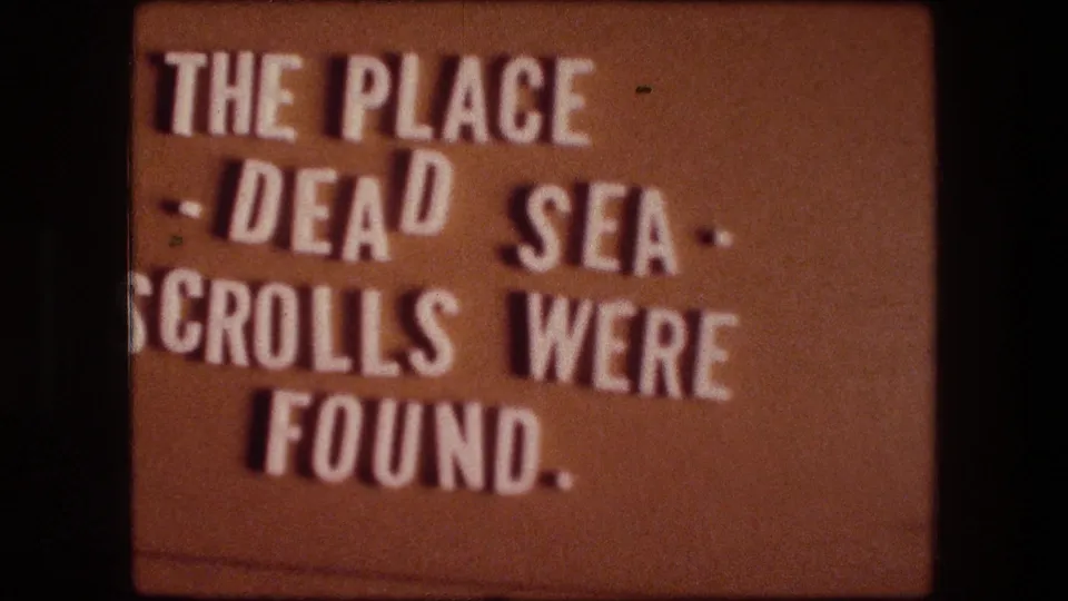 Final sampled frame of the 8mm title card, showing bold white text about the Dead Sea Scrolls against a brown card.