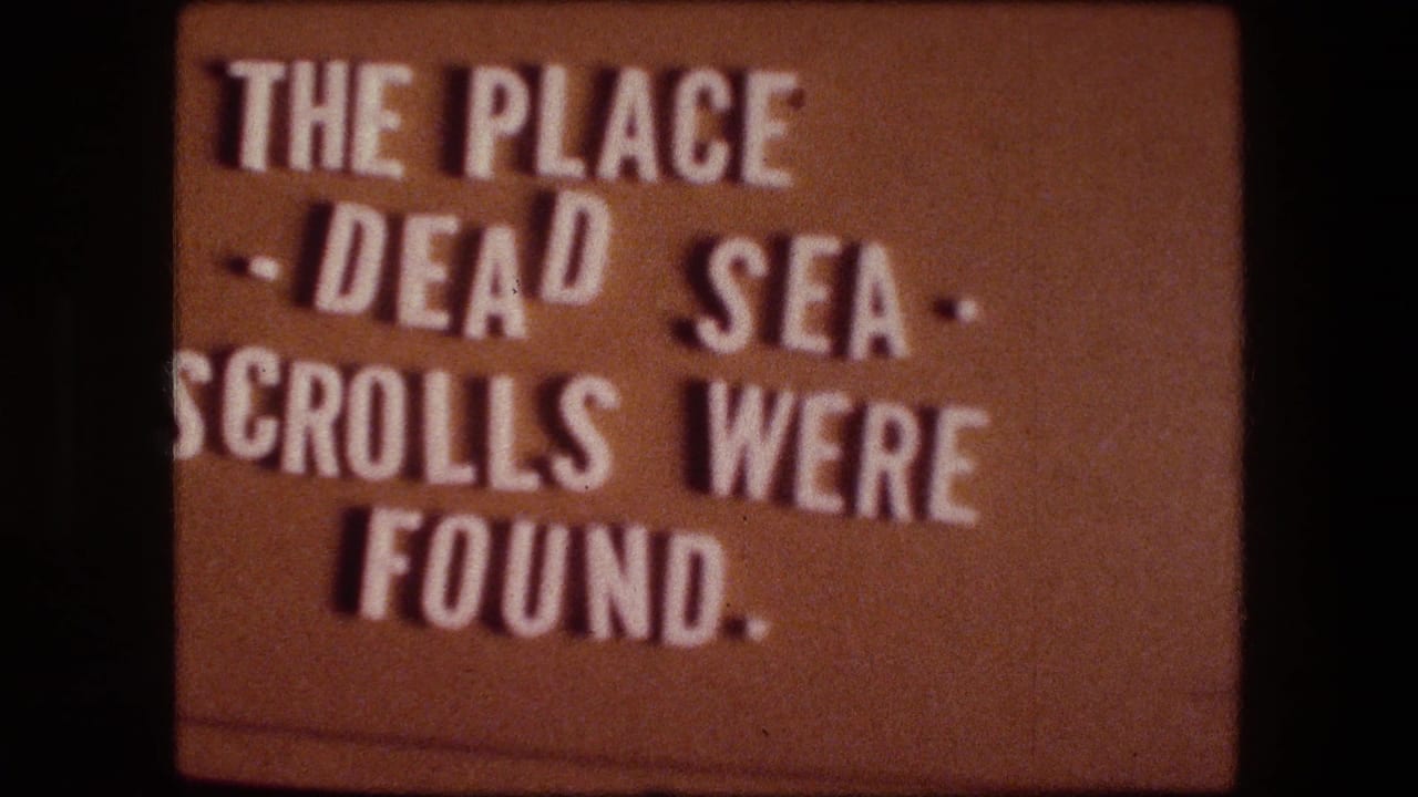 Warm-toned 8mm title card repeats the text about the Dead Sea Scrolls being found at this place.
