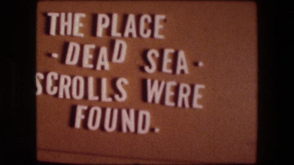 Warm-toned 8mm title card repeats the text about the Dead Sea Scrolls being found at this place.