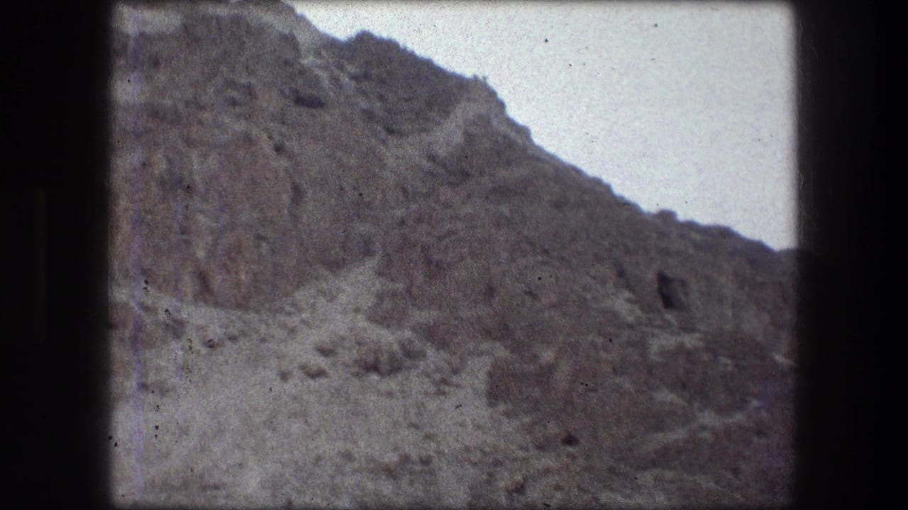 1976 8mm home-movie frame from Messada, Israel, showing a steep rocky hillside under a pale sky with soft grain and gate edges.