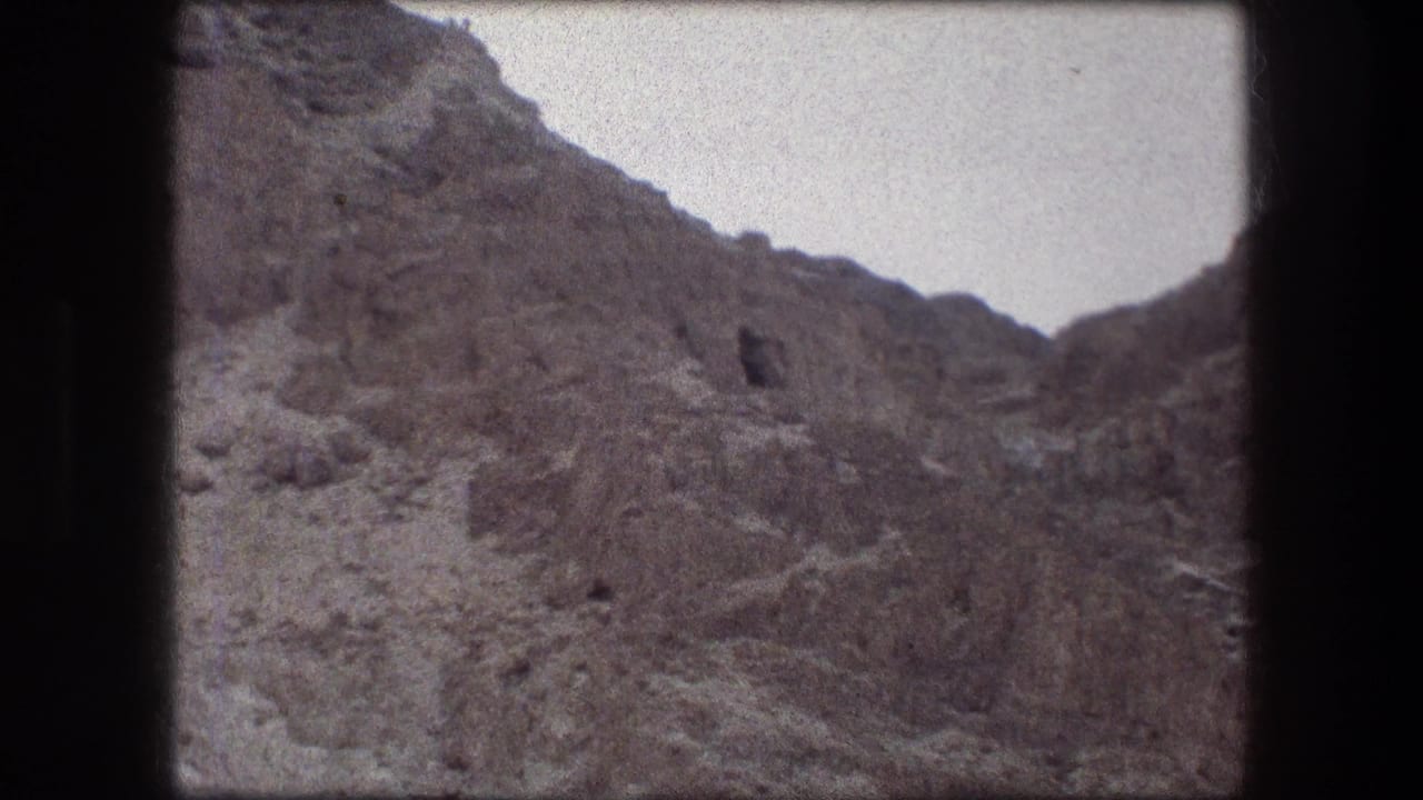 Steep brown rock face with a small dark opening and pale sky above.