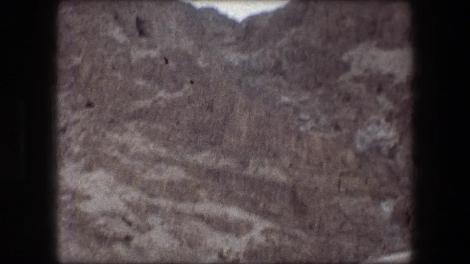 Grainy 1976 8mm view of rugged Messada terrain, with uneven rock textures and dry scrub filling the frame.