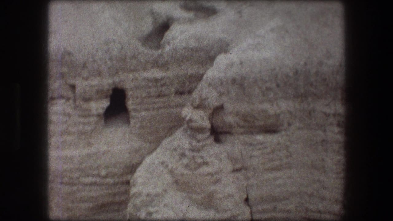 Eroded rock face with a dark opening set into a pale desert hillside.