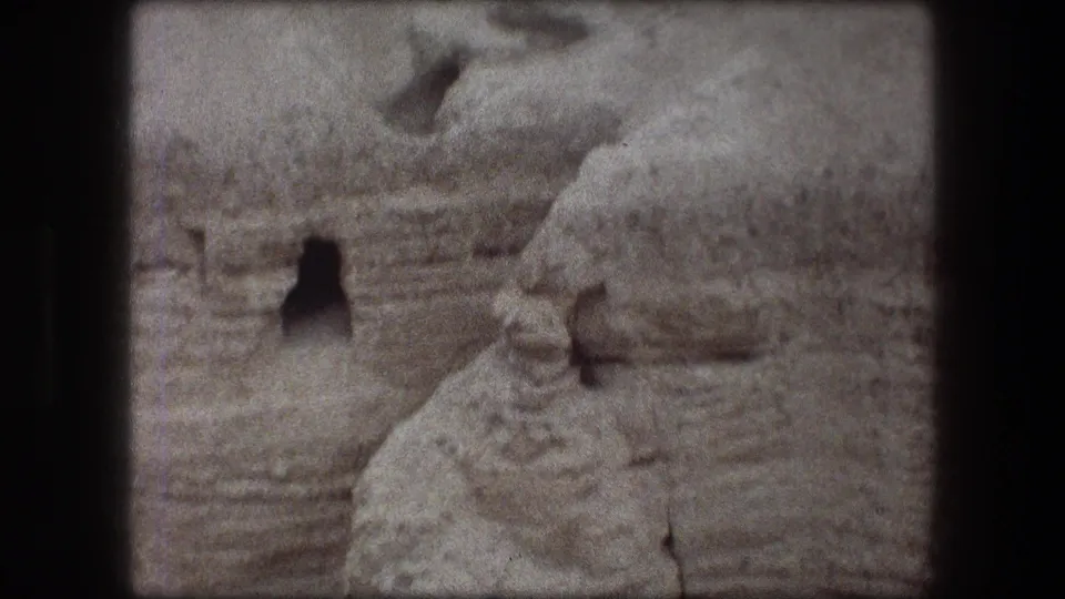 Messada hillside detail on 8mm film, showing pale eroded rock and a dark cave-like opening in the terrain.