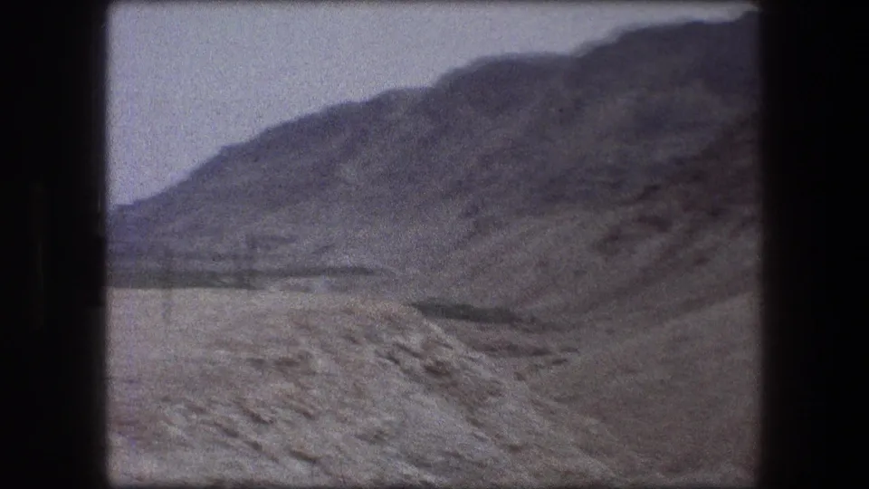 Wide 1976 8mm landscape view of Messada's arid hills, with muted color, soft focus, and a pale sky above the ridge.