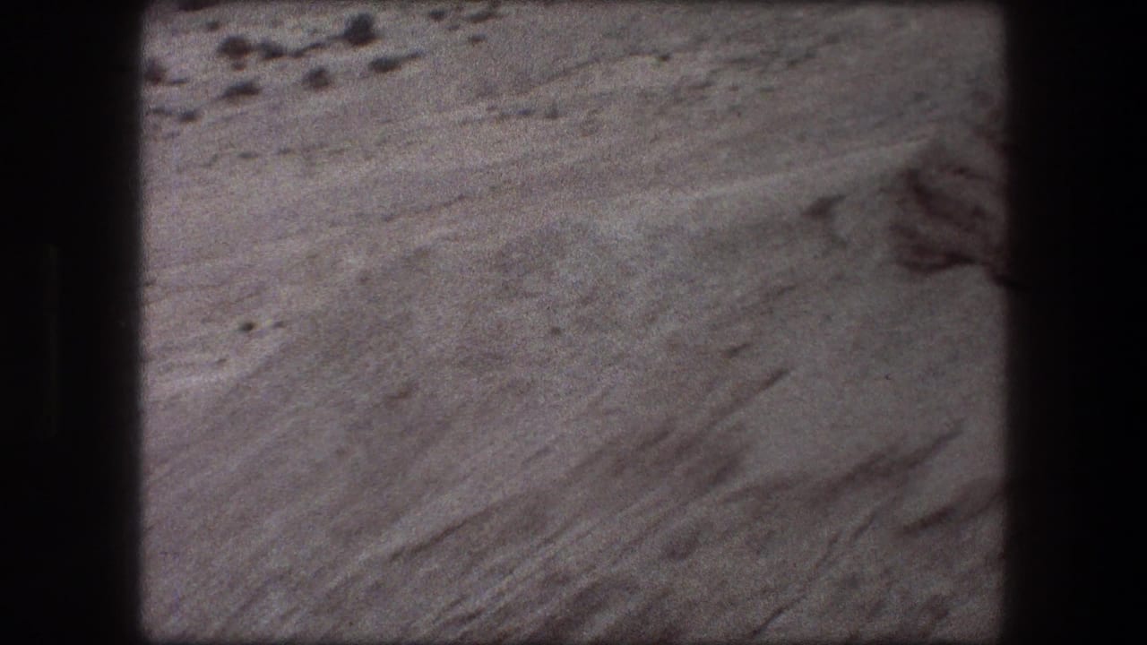 1976 8mm view from Messada, Israel, showing pale layered rock, scattered stones, and visible film gate edges.