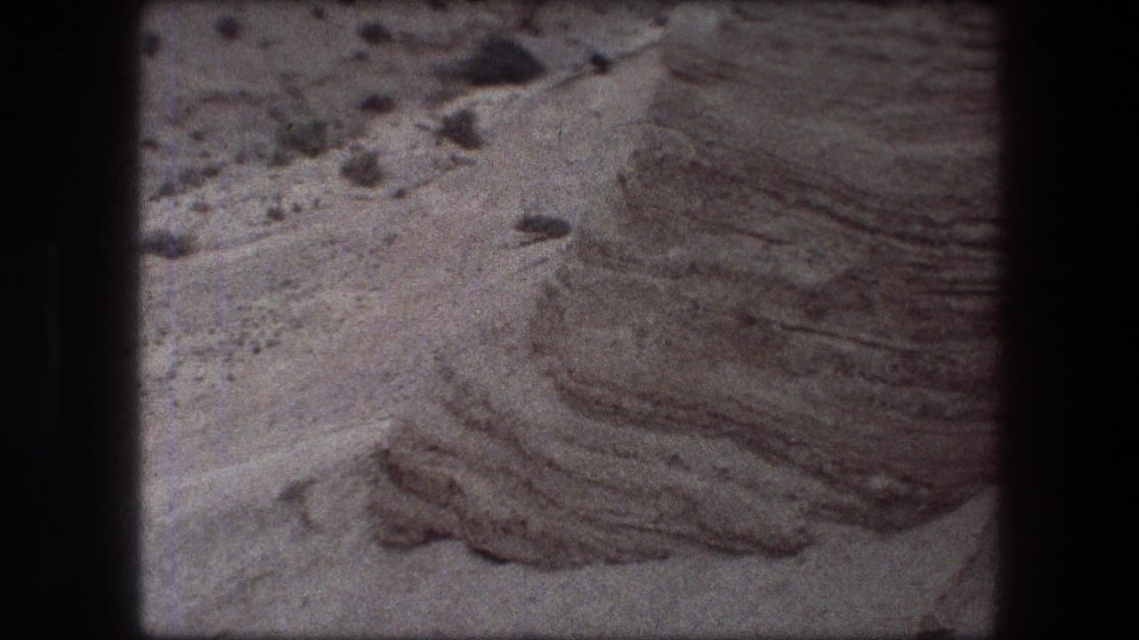 1976 8mm Messada, Israel frame showing a close rocky surface with rippled texture, loose stones, and dark scan borders.