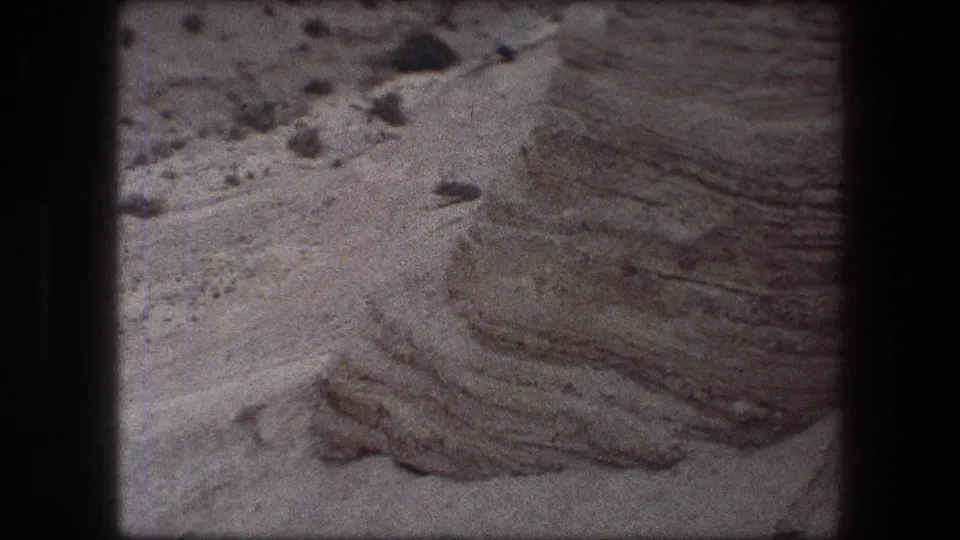 1976 8mm Messada, Israel frame showing a close rocky surface with rippled texture, loose stones, and dark scan borders.