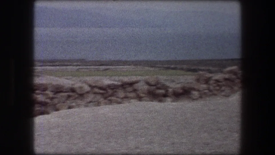 1976 8mm Messada, Israel view showing a low stone wall, open ground, distant hills, and a hazy desert horizon.