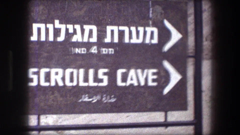 Close 8mm frame of the Masada Scrolls Cave directional sign, showing Hebrew, English, and Arabic text.