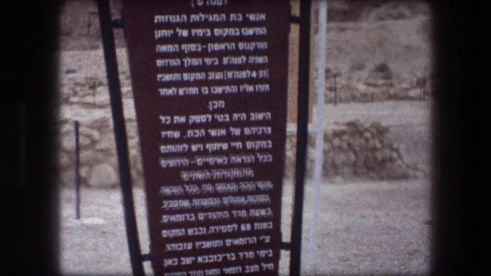 1976 8mm frame with the upper section of a Hebrew informational sign at Messada, partly cropped and softly focused.