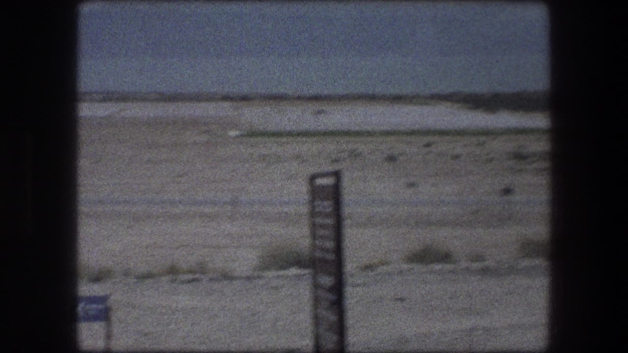 Zoomed 1976 Messada, Israel desert frame with a dark signpost in front of open arid terrain and low hills.