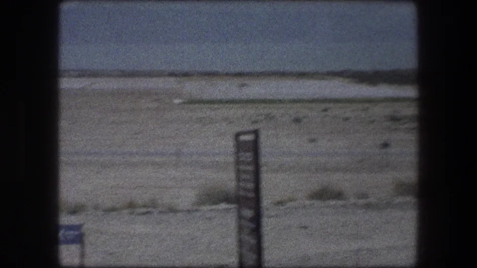 Zoomed 1976 Messada, Israel desert frame with a dark signpost in front of open arid terrain and low hills.