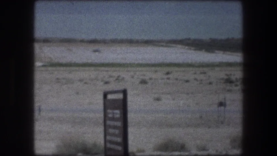 Late-frame 1976 Messada, Israel desert shot with foreground sign, sparse vegetation, and soft 8mm film texture.