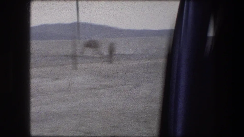 1976 8mm Messada, Israel travel frame showing a blurred arid landscape seen past a blue vehicle curtain.