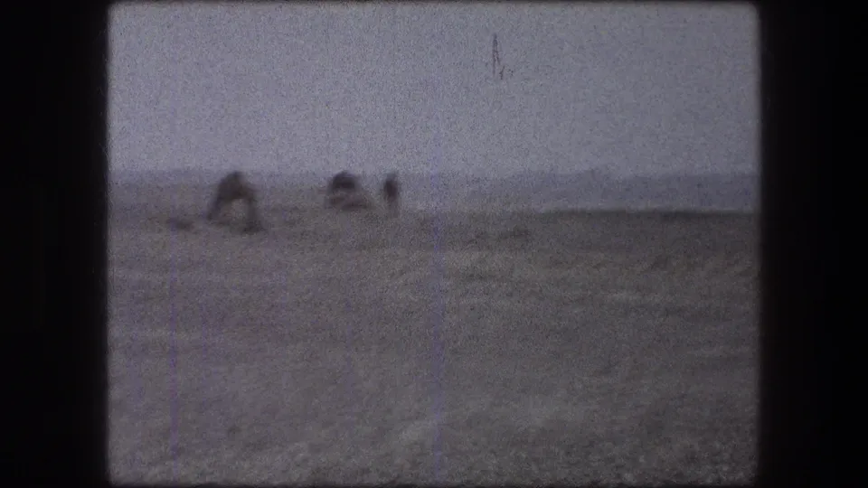 1976 Messada, Israel 8mm frame showing distant figures working in a dry field under a pale sky.