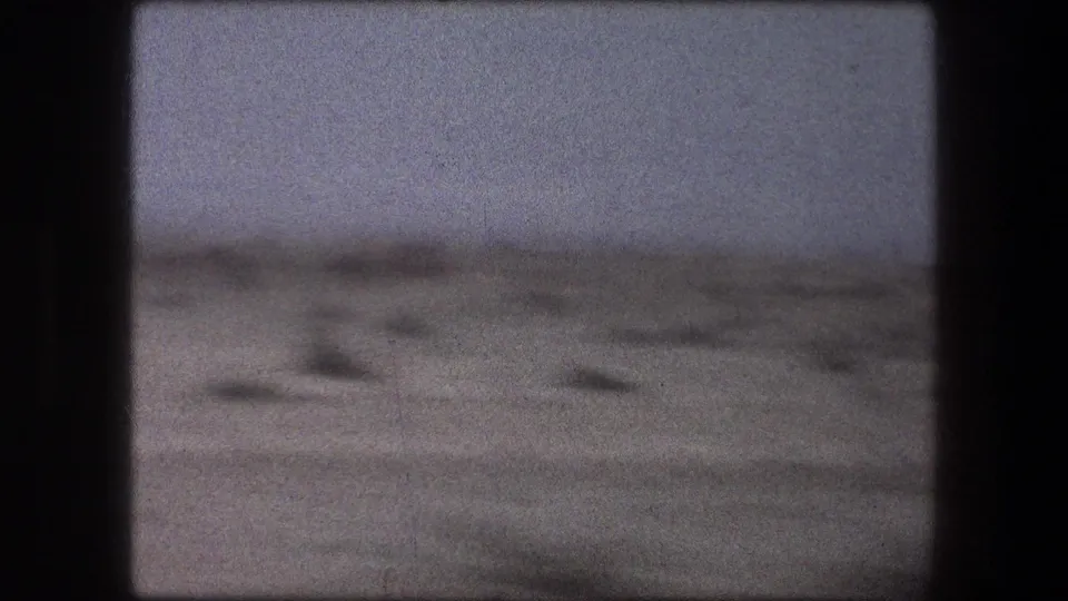 Soft 8mm frame from Messada, Israel showing open desert ground, scattered shrubs, and a hazy sky in 1976 footage.