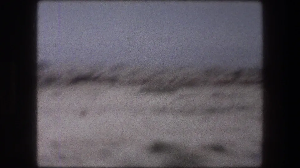 1976 8mm train-window view near Messada, Israel, showing hazy open ground and distant low terrain.