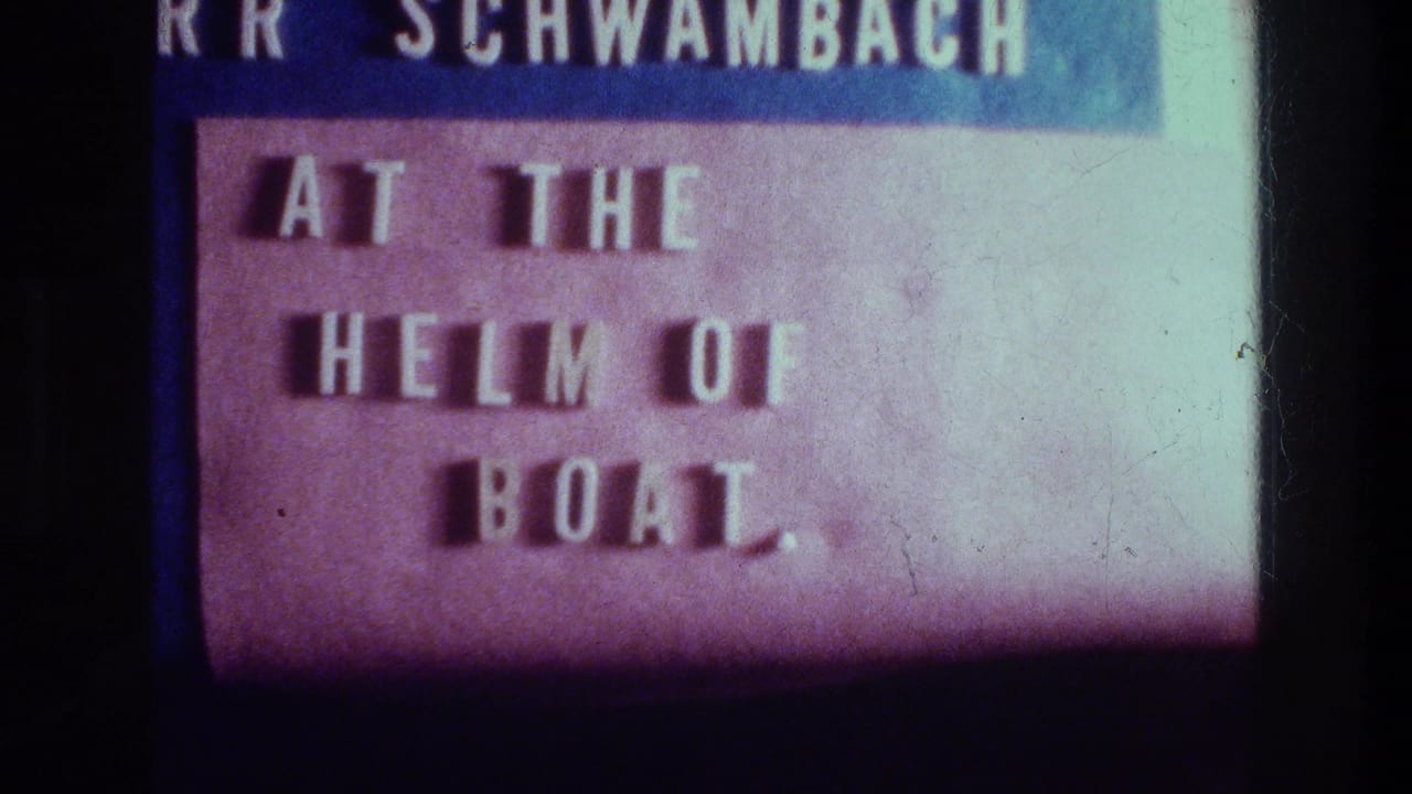 Projected 8mm title card showing a name line above the phrase “AT THE HELM OF BOAT.” in white letters.