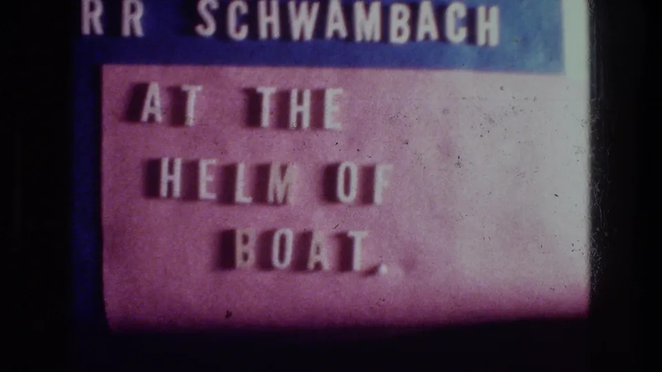 1976 8mm title card for a Sea of Galilee boat scene, reading “AT THE HELM OF BOAT” with a partial name above.