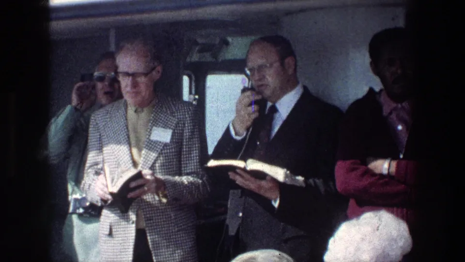 Inside a tour vehicle near the Sea of Galilee, a suited guide appears to lead a reading as passengers listen in close quarters.