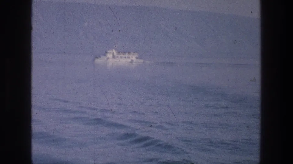A soft 8mm view of a distant white passenger boat on the Sea of Galilee, framed by dark vertical edges.