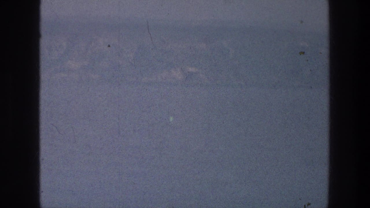 Hazy distant mountains and pale water framed by dark 8mm film edges.