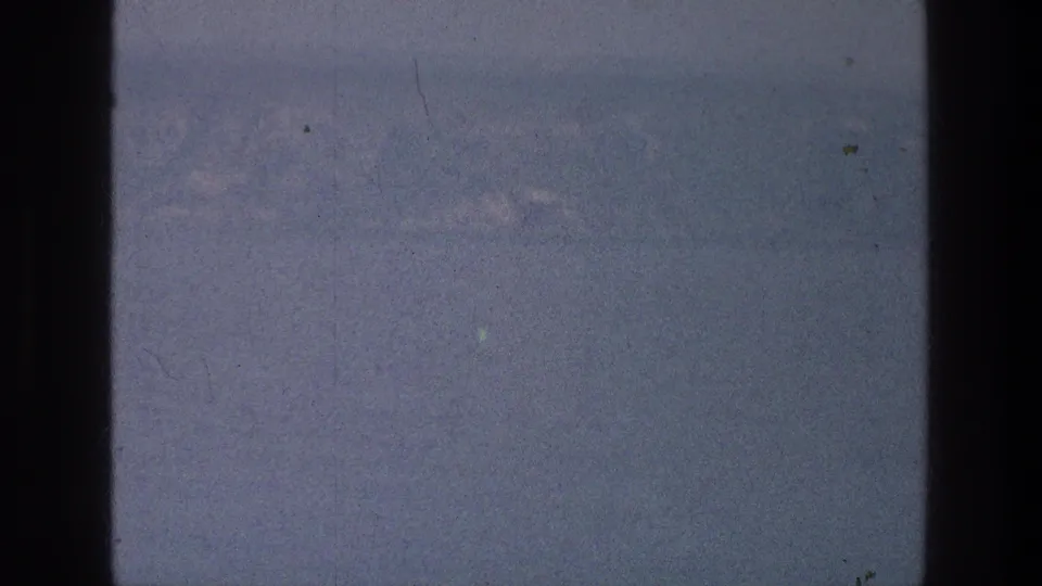 1976 8mm home-movie view of the Sea of Galilee area with faint mountains across pale water and dark gate borders.