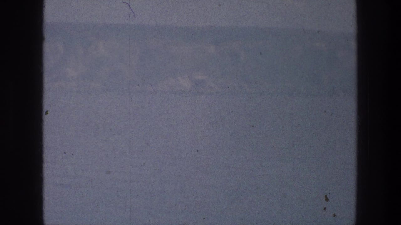 Pale blue-gray water and faint mountain ridge divided by a dark vertical film edge.